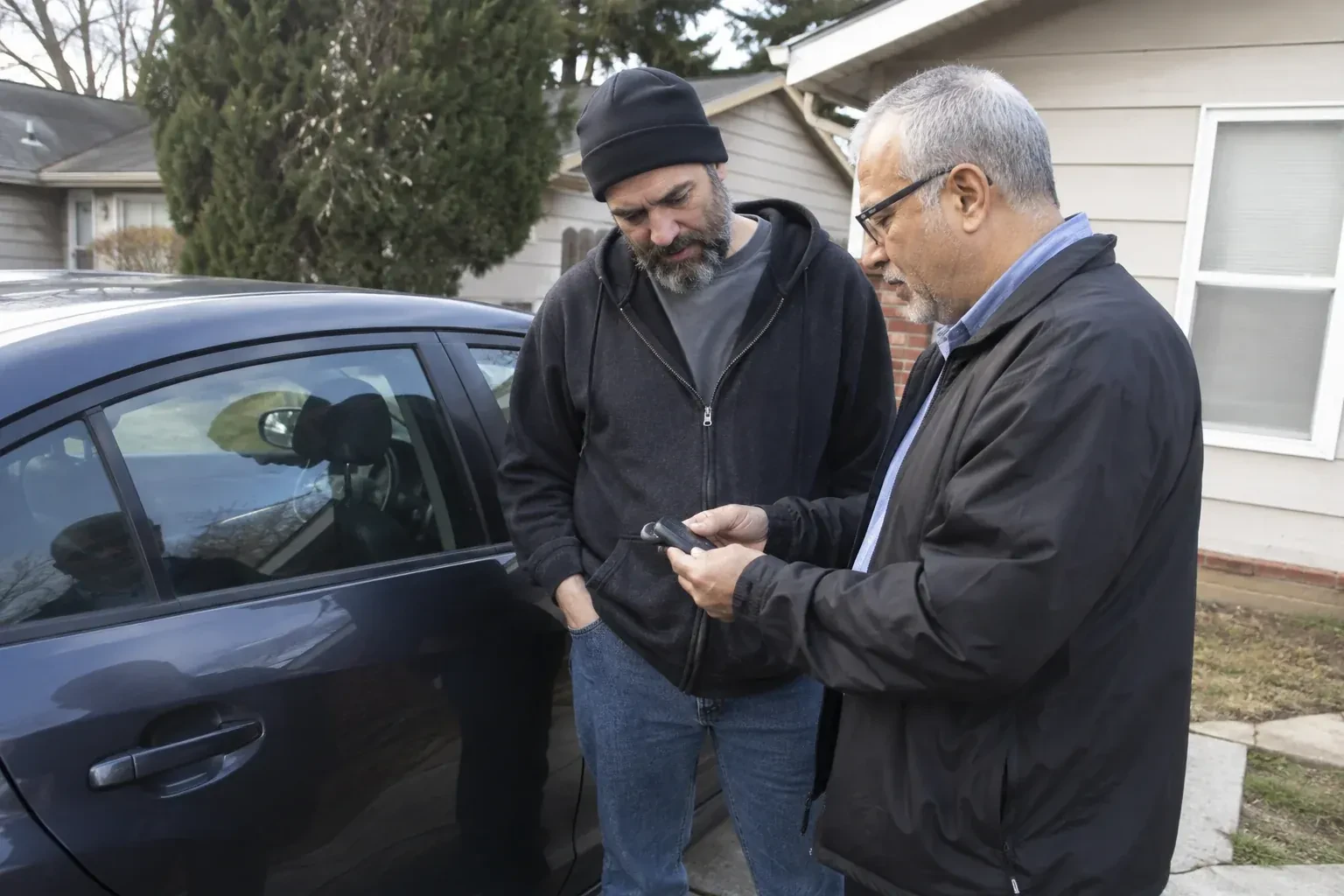 Two adults discussing a key fob beside a parked car. — Car Lockout Service, Newmarket