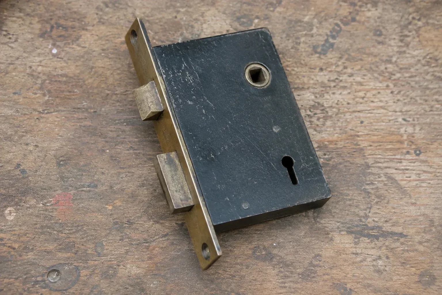 Closed mortise lock case with spindle opening, keyhole, latch and deadbolt on a wooden workbench. — Vintage Mortise Lock Service, Newmarket